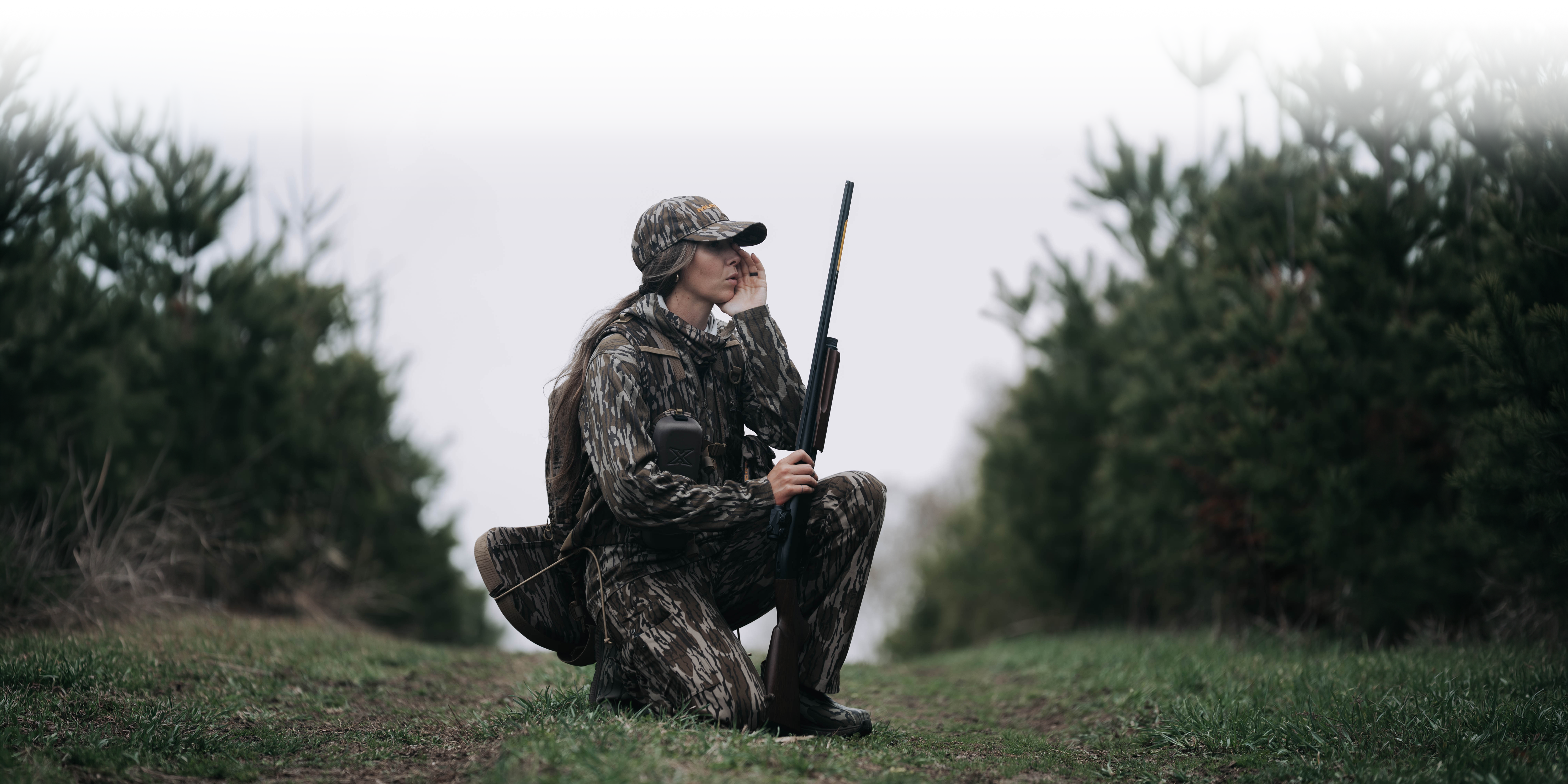Woman hunter kneeling in the field wearing Muddy camo
